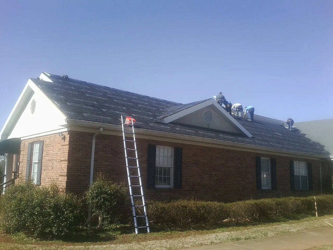 Crew tearing shingles off a brick ranch roof with a ladder set — Metal Roof Repair work by our crew in Bridgeport